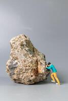 Tiny figurine of a man pushing a massive rock, symbolizing perseverance, struggle, and determination. photo