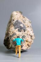 A tiny figurine a man pushing a massive rock, symbolizing perseverance, struggle, and determination. photo