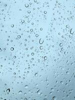Water droplets scattered across a glass surface with a soft blue sky behind. photo
