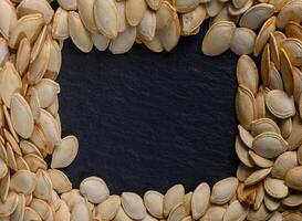 Pumpkin seeds arranged in a decorative frame on a dark slate background for autumnal culinary inspiration photo