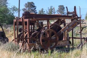 Rusty vintage machinery stands abandoned in a field under the clear blue sky at midday in a rural setting photo