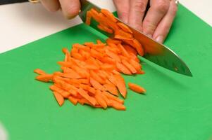 Hands skillfully slice vibrant orange carrots on a green cutting board, adding color to a culinary creation photo