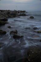 Gentle waves caress rocky shore under soft twilight sky during evening calmness by the seaside photo