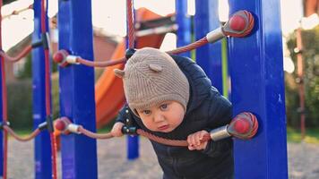 One year old boy in a black jacket runs and plays outside on the playground. Child learns the world. Toddler boy smiles and has fun on the playground. video
