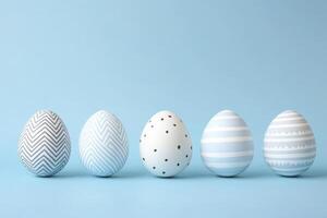 Five delicately decorated Easter eggs in calming pastel hues line up against a soft blue background, a peaceful spring scene symbolizing new beginnings and hope. photo
