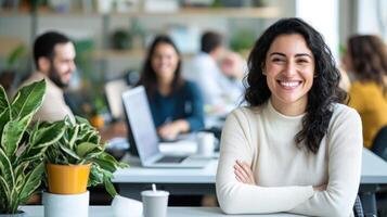 Portrait of a desk businesswoman sitting at her smiling with a laptop in a bright modern office, her colleagues are working in the background photo