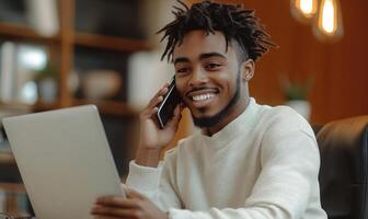 working black man talking Young mobile smartphone and on on laptop, smiling in home office with plants photo