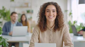 Portrait of a smiling businesswoman sitting at her desk with a laptop in a bright modern office, her colleagues are working in the background photo
