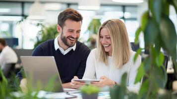 man and woman share a laugh while working at and desks in a contemporary office. They look at a tablet together, creating a collaborative their friendly work environment photo