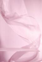 Empty glass shelf with flowing pink cloth backdrop creating a soft, elegant setting, ideal for showcasing products or creating a minimalist aesthetic photo