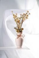 Dried daisy flowers arranged in a simple vase with a white background and soft draping fabric create a serene and elegant still life composition, emphasizing natural beauty and simplicity photo