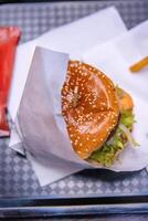 Top view of a delicious burger with sesame seed bun, fresh lettuce and tomato wrapped in paper, Closep of hamburger on the tray on the table in fast food restaurant. 2 photo
