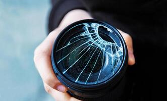 Closeup of a hand holding a broken shattered camera lens with visible cracks, symbolizing damage and fragility of photography equipment, repair or replacement needs, accidents, or fragility. 01 photo