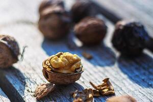 Closeup of cracked open walnut with exposed kernel on rustic wood, surrounded by whole nuts and shells. Fresh walnut half with visible nutmeat on textured wooden surface. Selective focus photo