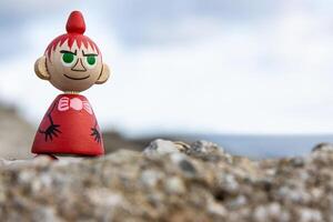 Tallinn, Estonia. September 1st, 2024. Wooden figure of Little My placed on a rock by the sea, symbolizing nordic literature, whimsical characters, and timeless charm of Tove Jansson moomin creations photo