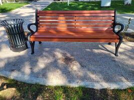 On a clear sunny spring day, there is a new urn and a brown bench in a shady park photo