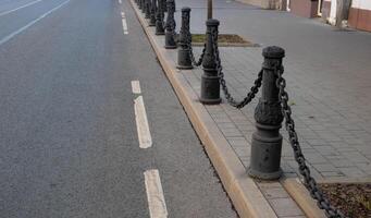 Black wrought iron poles with chains, fences by the road. An old, rare fence. photo