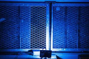 Metal grid illuminated by dramatic eerie blue light, creating a mysterious, gritty urban atmospher. Metallic fence, symbolizing security, restriction, protection and industrial aesthetics 02 photo