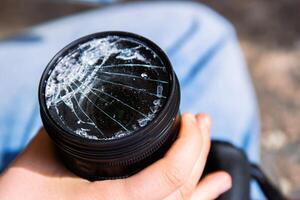 Closeup of a hand holding a broken shattered camera lens with visible cracks, symbolizing damage and fragility of photography equipment, repair or replacement needs, accidents, or fragility. 04 photo