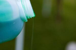 Closeup of vibrant green detergent pouring from a white plastic bottle against a blurred background. Green liquid flowing from a container. Copy space. Selective focus 01 photo