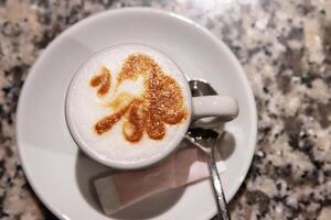Top view of a cappuccino with intricate latte art in a white ceramic cup on a marble table, served with a spoon and sugar, Coffee culture, creativity, barista skills concept and cozy cafe 01 photo