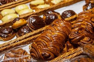 Assortment of freshly baked challah loaf and golden brown pastries with vanilla and chocolate toppings displayed in rustic woven wicker baskets on the shelf on grocery department in supermarket. 03 photo