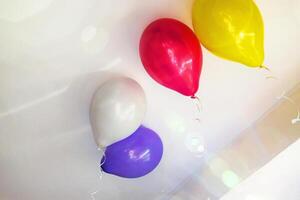Group of multicolored vibrant helium balloons with ribbons in red, purple, yellow, and white hanging from a ceiling, perfect for party themes or event decorations. Copy space 02 photo