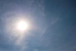 Bright sun shining through wispy clouds in blue sky photo
