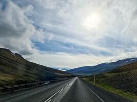 Empty asphalt road crossing Iceland landscape under cloudy sky photo