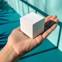 White Cube Held by a Hand on Aqua Background with Harsh Shadows and Bright Daylight photo