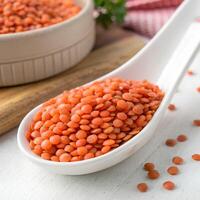 Red Lentils in White Spoon on Textured White Table With Bowl and Wood Block photo