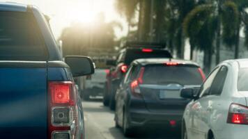Rear side of blue pickup car with turn on brake light. Many car queue up due to traffic congestion. Side road with trees. Background of bright light of the sun shines. photo