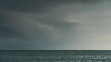 Vast expanse blue water of ocean under a cloudy overcast sky. Horizon line is visible with faint landmasses in the distance. The scene is moody and atmospheric before heavy rain. photo