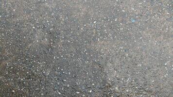 Textured surface of asphalt road. Rough grainy texture is visible with small pebbles or aggregate embedded in the gray material. Focus is on the surface texture and detail of water from rain on top. photo