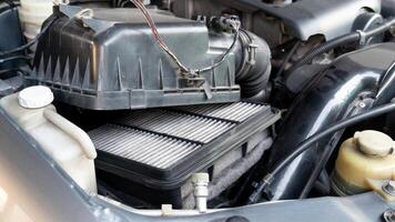 Vehicle engine compartment change equipment activity. Focus is on used rectangular air filter positioned within a black plastic housing. Various other engine components including hoses and wires. photo