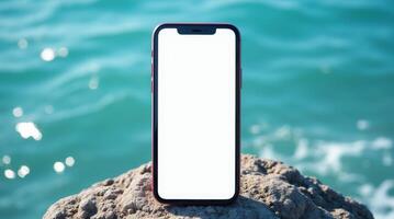 Smartphone with blank white screen standing on rock near water. Mockup for digital advertising, mobile apps, or outdoor technology photo