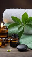 Spa composition with green towels, essential oil bottles, burning candle, black massage stone and green leaves on wooden surface photo