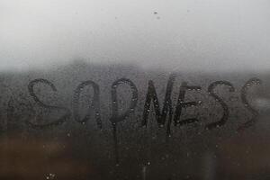 The inscription sadness on the wet window. photo