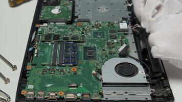 Skilled technician performs maintenance on a laptop motherboard, carefully handling components in a well-lit workshop. Tools are arranged nearby for easy access. video