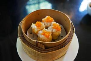 Close up Pork and Shrimp Shumai Dim Sum, Chinese dumplings served in steamed wooden basket container photo