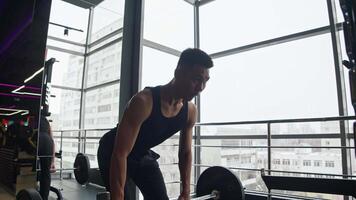 pectoral muscles of the Asian athlete performing Romanian deadlift in gym with barbell are visible. He concentrates and looks in mirror, carefully watching his form and technique. video