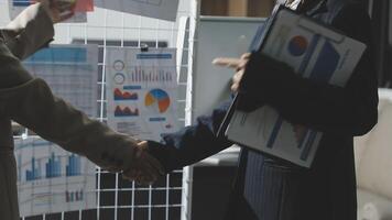 Two business people shaking hands in front of a board with graphs video