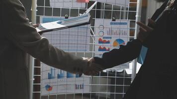 Two business people shaking hands in front of a wall of graphs video