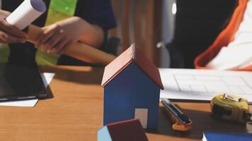 A man is working on a house model with a laptop video