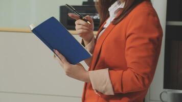 A woman in an orange blazer holding a notebook video