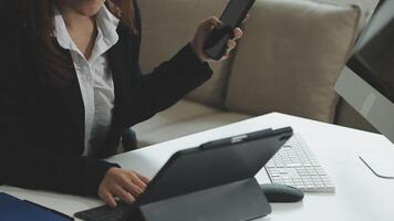 A woman in a business suit is using her phone and laptop video