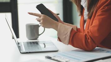 A woman in an orange jacket is using her phone while sitting at a desk video