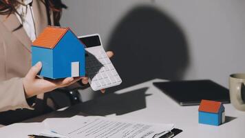 A woman holding a house model in front of a calculator video
