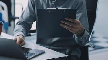 A man is working on his laptop while holding a clipboard video