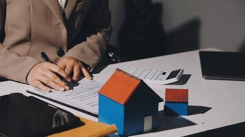 A woman in business suit writing on a paper with a pen and a house model video